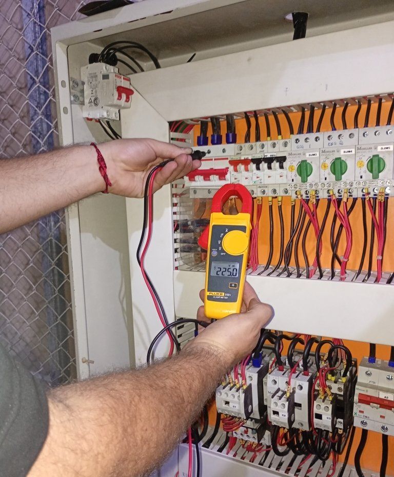 Técnico medindo corrente com alicate amperímetro em quadro de bombas